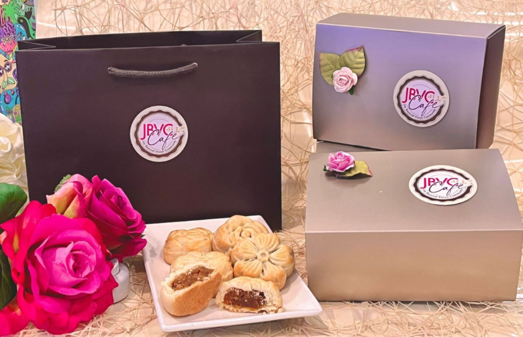 Image describing some pineapple cakes serving on a plate with 2 red roses on the left and 2 gift boxes on the right and a gift bag behind